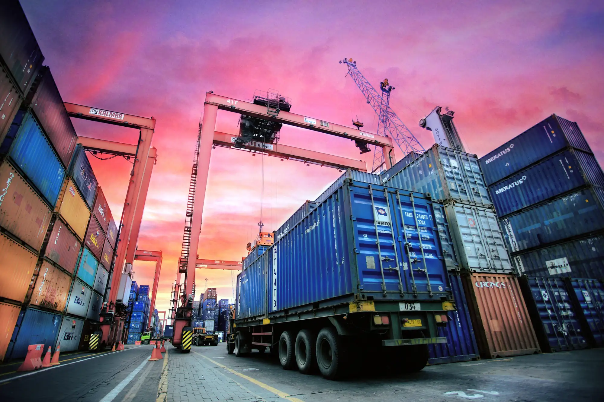 Stacked shipping containers and a loaded truck at a port at dusk.